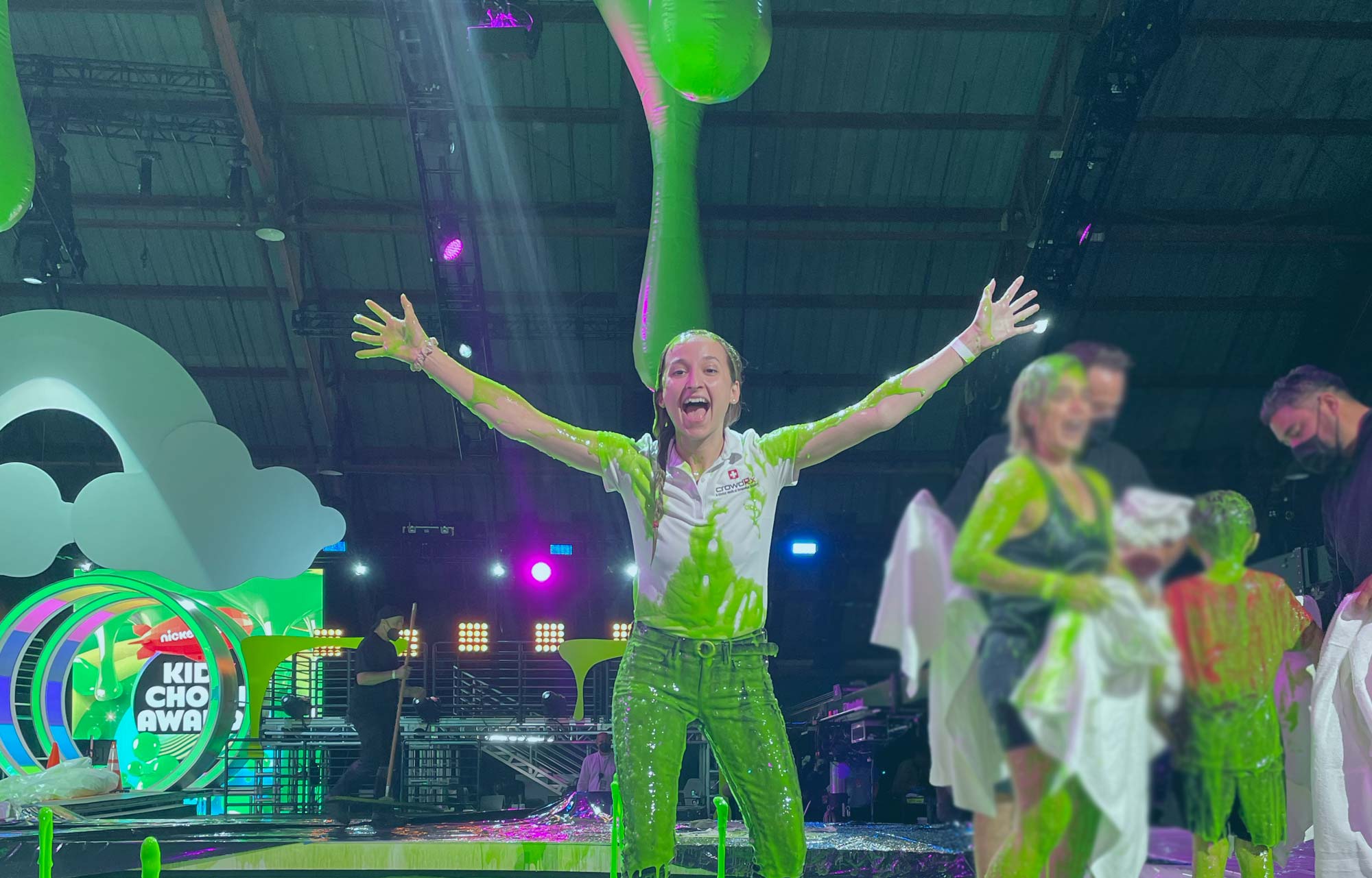 Staff member having pretend slime dumped on her head. She is smiling and holding her arms up